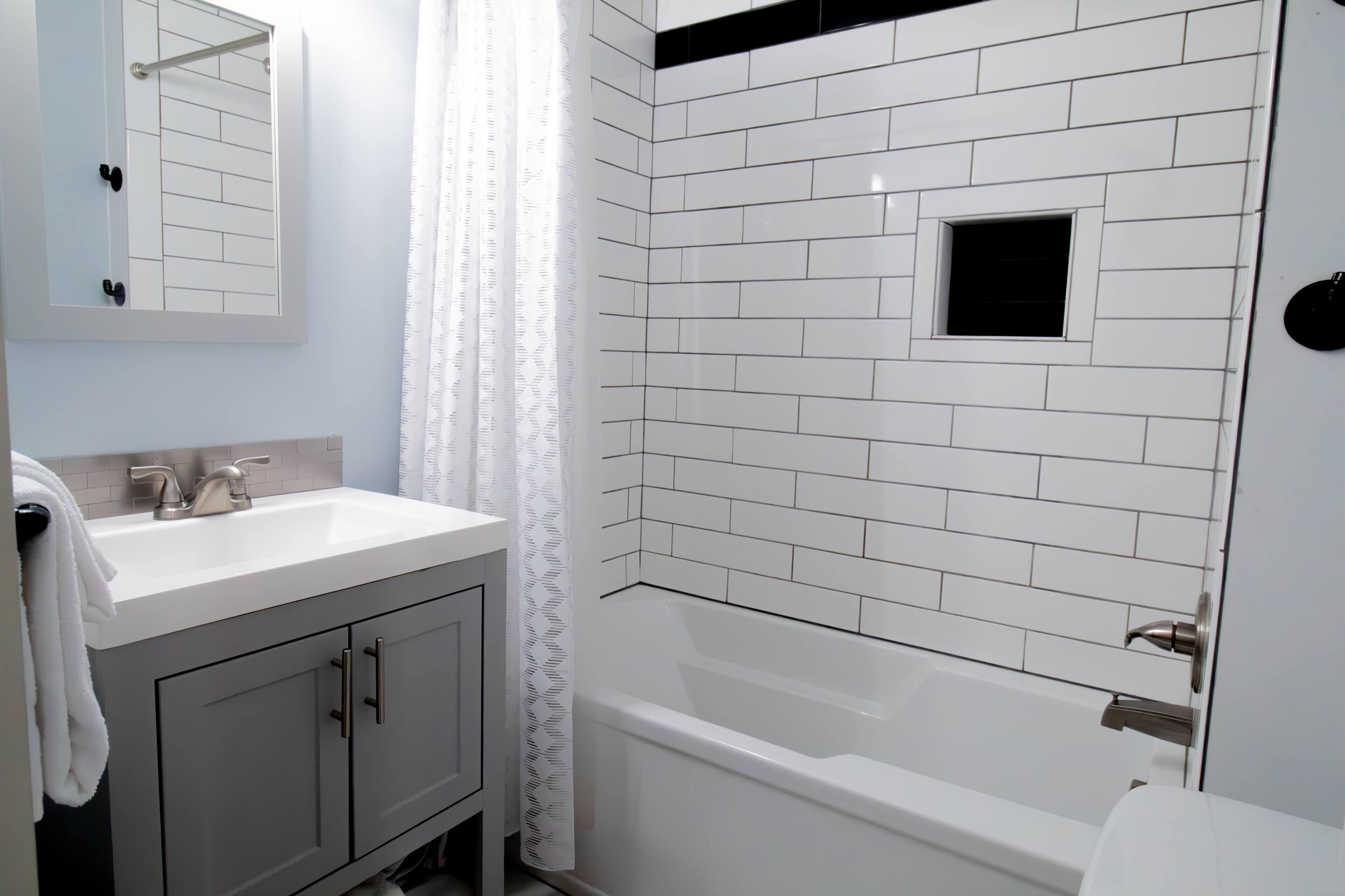 A bathroom with white tiled walls, a white sink, and a bathtub.