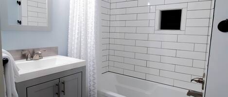A bathroom with white tiled walls, a white sink, and a bathtub.