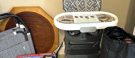 A room with a wooden floor, a patterned ironing board, a suitcase, and Monopoly game boxes.