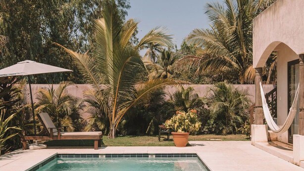 Ein Pool mit Fliesenrand, umgeben von Palmen und einer Hängematte.