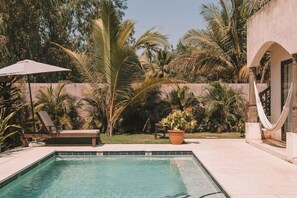 A swimming pool with a tiled edge, surrounded by palm trees and a hammock.