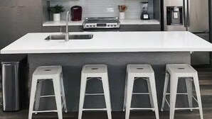 Una cucina moderna con isola centrale, elettrodomestici in acciaio inossidabile e tre sgabelli bianchi.