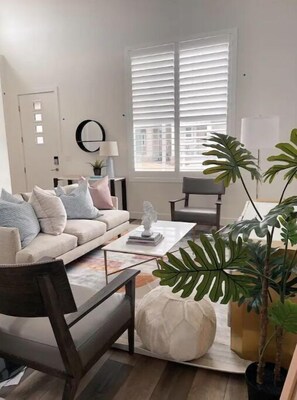 A modern living room with a sofa, coffee table, and chairs. There is a window with blinds, a lamp, and a potted plant. - Just Listed! 4 Bed Lux Modern Rambler, Ultra Clean, Office, Centrally located! (Bluffdale)