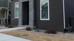 Una casa moderna a due piani con facciata scura, un muro in pietra decorativo e un piccolo portico.
