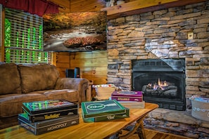 A cozy living room with a stone fireplace, leather sofa, and board games.