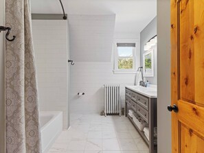 A bathroom with a shower, a bathtub, a toilet, a sink with a mirror, and a window.