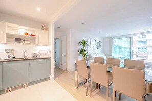 A modern kitchen with grey cabinets, a dining area with a table and chairs, and a large window providing a view of the city.