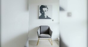 Een moderne kamer met een grijs gestoffeerde fauteuil, een witte muur en een kunstwerk in een lijst.