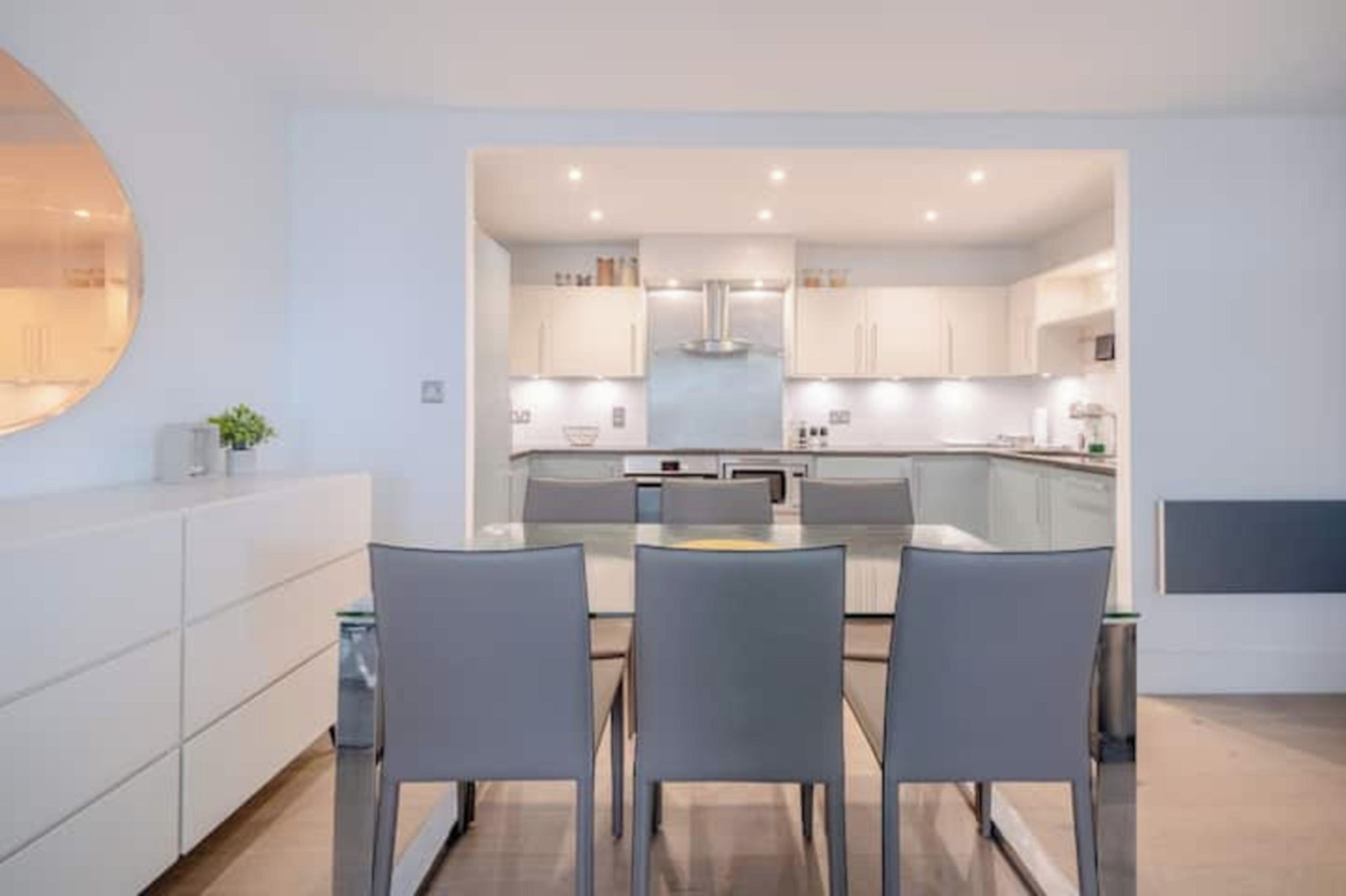 Cocina moderna con una isla central, armarios blancos y una zona de comedor con dos sillas.
