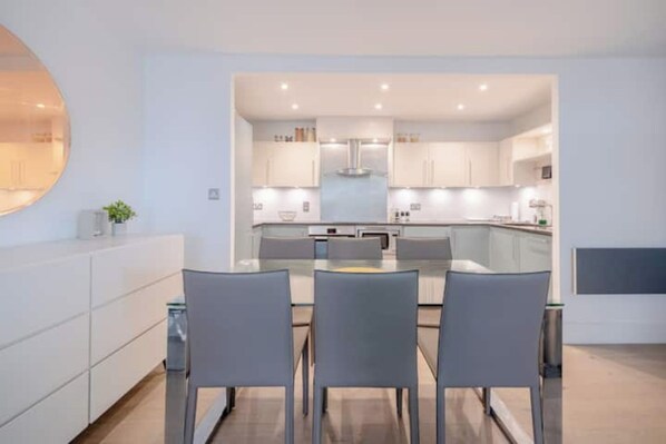Cocina moderna con una isla central, armarios blancos y una zona de comedor con dos sillas.