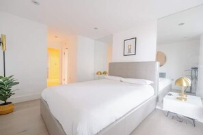 Une chambre moderne avec un grand lit, des tables de chevet, un miroir et une plante en pot.