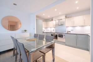 Une cuisine moderne avec des meubles blancs, une table à manger en verre et un grand miroir rond accroché au mur.