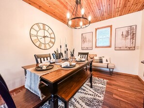 A dining room with a wooden table, chairs, a large wall clock, and framed artwork.