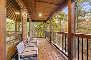 A wooden deck with a railing, a covered area with seating, and a view of trees.