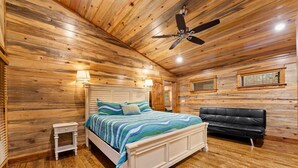 Een slaapkamer in een blokhut met een bed, nachtkastje en een zwarte leren bank.
