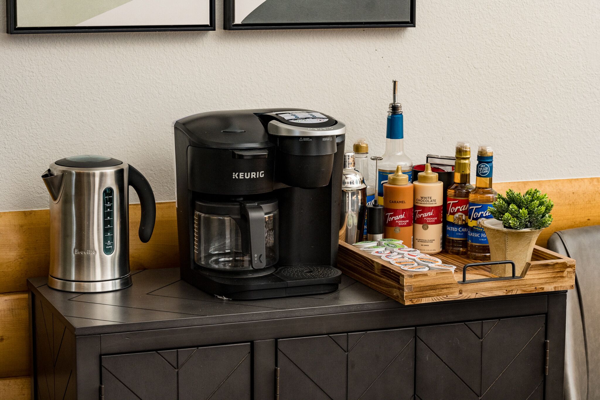 Une petite cuisine équipée d’une machine à café Keurig, d’une cafetière Breville et d’un plateau contenant des sirops Torani et d’autres condiments.
