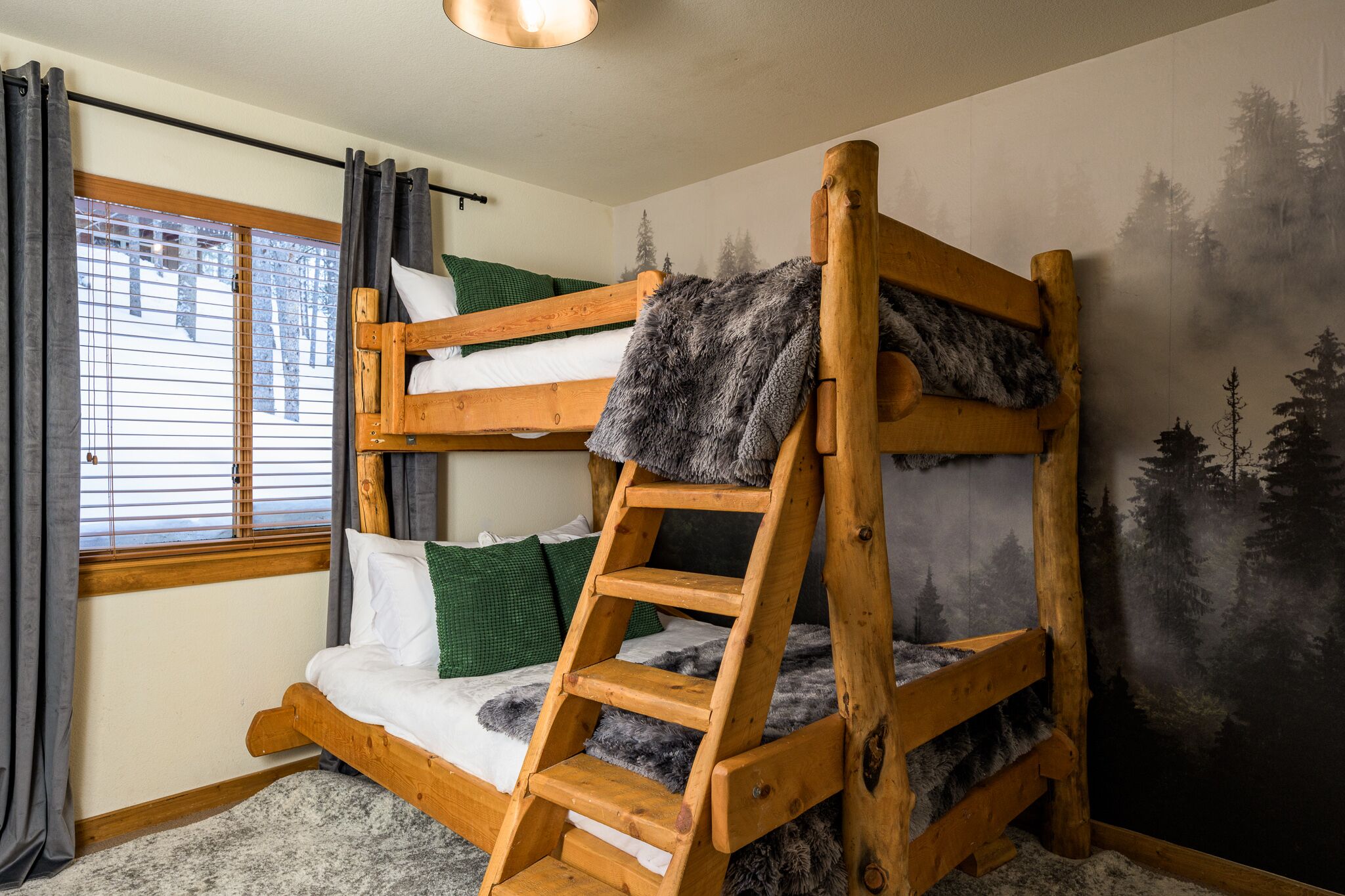 A bunk bed with a ladder, a window with curtains, and a forest mural on the wall.