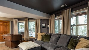 A modern living room with a sectional sofa, a foosball table, and large windows with curtains.