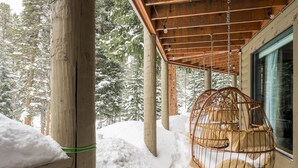 A wooden structure with a hanging birdcage chair, snow-covered ground, and a window with curtains.