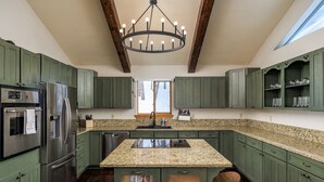 A kitchen with green cabinets, stainless steel appliances, granite countertops, and a central island.