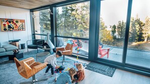 Een moderne woonkamer met grote ramen, een bank, een salontafel en een houten stoel.