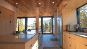 Een moderne keuken met houten kastjes, een centraal eiland en grote ramen met uitzicht op de omgeving.