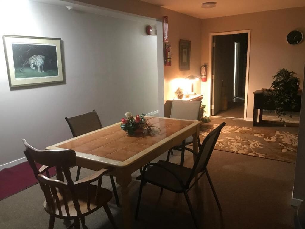 Uma sala de jantar com uma mesa e cadeiras de madeira, um quadro na parede e uma planta no canto.