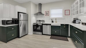 A modern kitchen with white cabinets, stainless steel appliances, and a window with blinds. - Fun, family friendly stay in Niagara Falls (Niagara Falls)