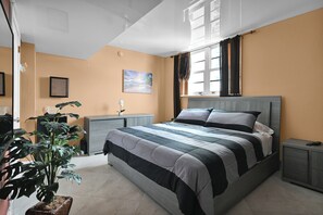 Un dormitorio con una cama grande, una mesita de noche, una planta en maceta y una ventana con cortinas.