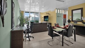 A modern office space with a glass partition, a brown sofa, a dining table with chairs, and a large window with a city view. - Direct access to beach and heated pool at The Tides (Hollywood)