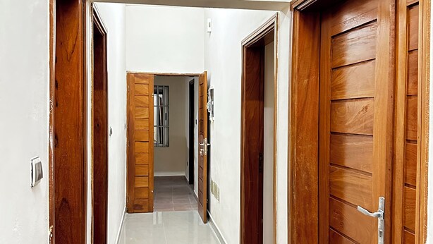 A corridor with wooden doors on both sides, leading to a room with a tiled floor and a visible window. - Cozy Room In Cotonou City
 (Cotonou)