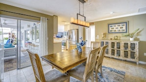 A dining area with a wooden table and chairs, a kitchen in the background, and a view of the outdoors. - Tropical Family Pool Home Near Siesta Key Beach | Sleeps 9 Dog Friendly,( Check restrictions)| Gulf Gate Sarasota | Sleeps 9 (Sarasota)