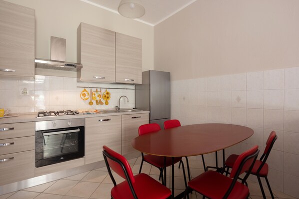 A modern kitchen with a built-in oven, a gas stove, and a stainless steel refrigerator. There is a round table with four red chairs.