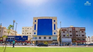 Ένα ξενοδοχείο με μια εντυπωσιακή μπλε πρόσοψη, που βρίσκεται σε κεντρικό σημείο και περιβάλλεται από άλλα κτίρια και σταθμευμένα αυτοκίνητα.