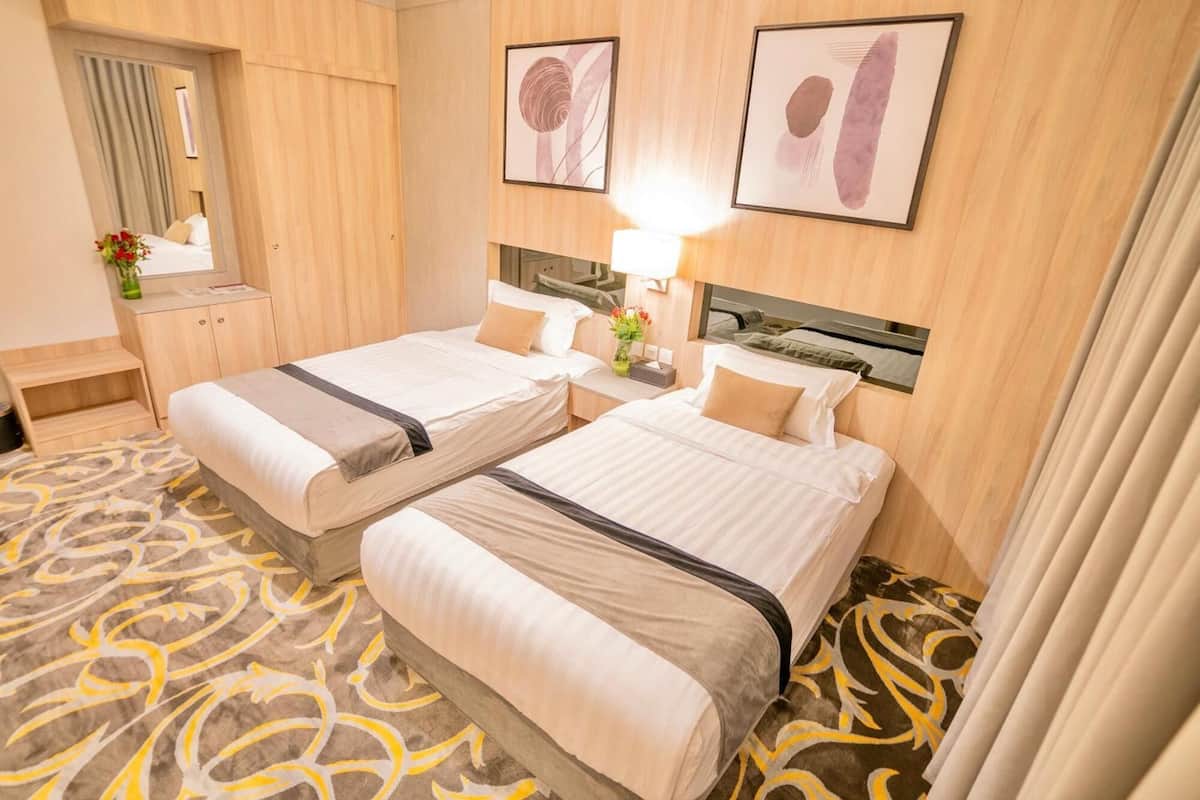 A hotel room with two beds, a wooden headboard, a mirror, and a patterned carpet.