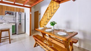 A kitchen with wooden beams, a dining table set with plates and glasses, and a staircase with a wooden railing. - Brisamar (Ubatuba)