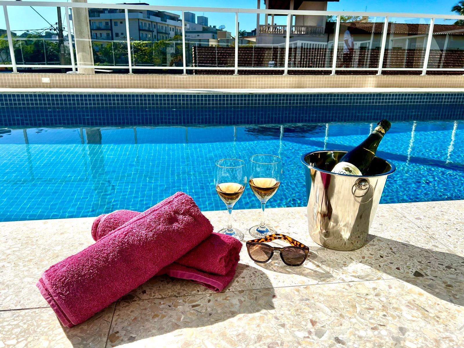A poolside setting with a champagne bottle, glasses, and a pink towel.