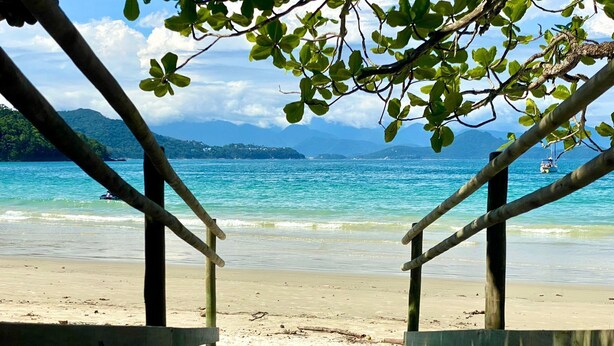 A wooden deck leading to a beach with clear turquoise water and distant mountains. - Brisamar (Ubatuba)