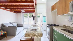 A modern kitchen with wooden beams, a dining area with a sofa, and a view to the outside. - Brisamar (Ubatuba)