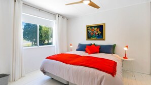 Ein modernes Schlafzimmer mit einem großen Bett, einem Deckenventilator, einem Fenster mit Vorhängen, einem Nachttisch mit Lampe und einem Bild an der Wand.