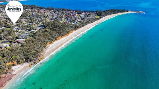 Luftaufnahme von Jervis Bay mit einem langen, schmalen Strand und einer dicht besiedelten Wohngegend.