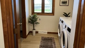 A laundry room with a washing machine, a potted plant, a window, and a rug.