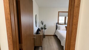 A narrow hallway leading to a bedroom with a bed, a dresser, a mirror, and a potted plant.