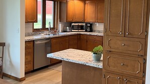 A kitchen with wooden cabinets, a granite countertop, a dishwasher, a microwave, and a coffee maker.