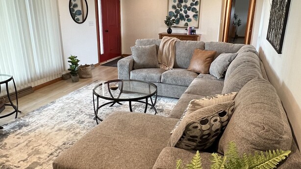 A living room with a sectional sofa, a glass coffee table, and a large fern plant.