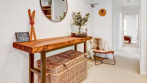 A hallway with a wooden console table, a mirror, a decorative plant, a chair, and a sign on the wall.