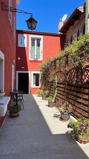 A narrow alleyway with a red building, a wooden fence, and potted plants.