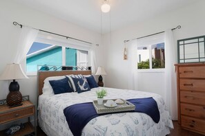 Un dormitorio con cama, dos mesitas de noche, cómoda y ventanas con cortinas.