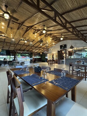 Une vaste salle à manger dotée d’un haut plafond et de poutres apparentes, où trône une longue table en bois, dressée pour un repas.