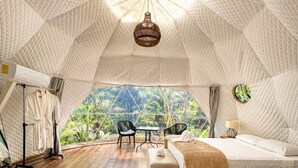Una habitación con techo abovedado, una cama, una mesa y sillas, con vistas a la vegetación exterior.